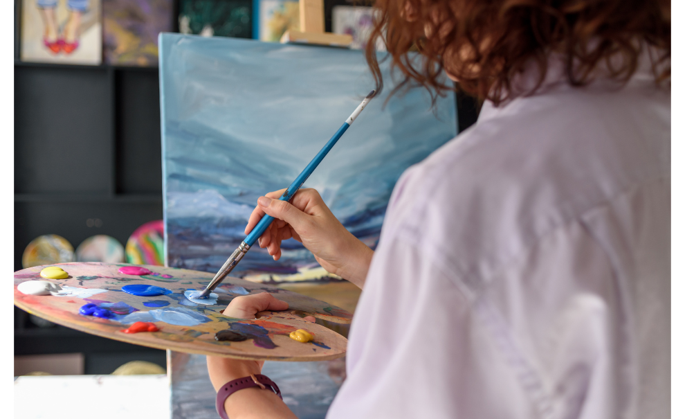 woman using a painting palette while in front of a canvas on an easel