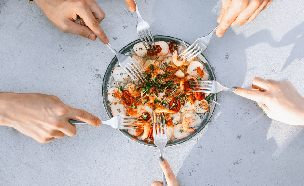 Hands holding forks reaching into a shared bowl of food