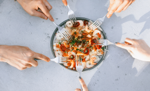 Hands holding forks reaching into a shared bowl of food