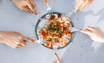 Hands holding forks reaching into a shared bowl of food